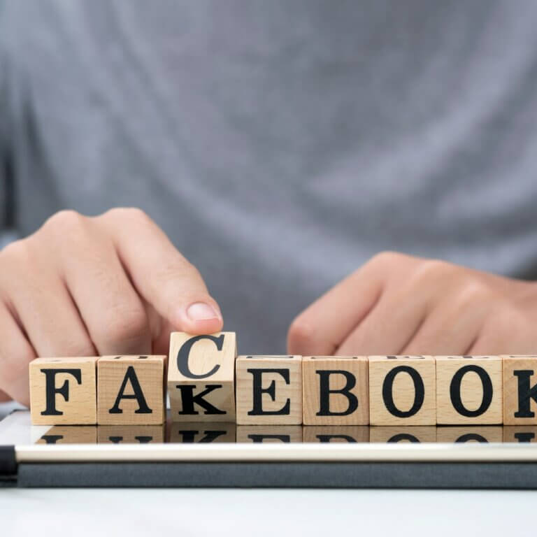 Hand flipping wooden woording for change "fakebook" to "facebook" on tablet